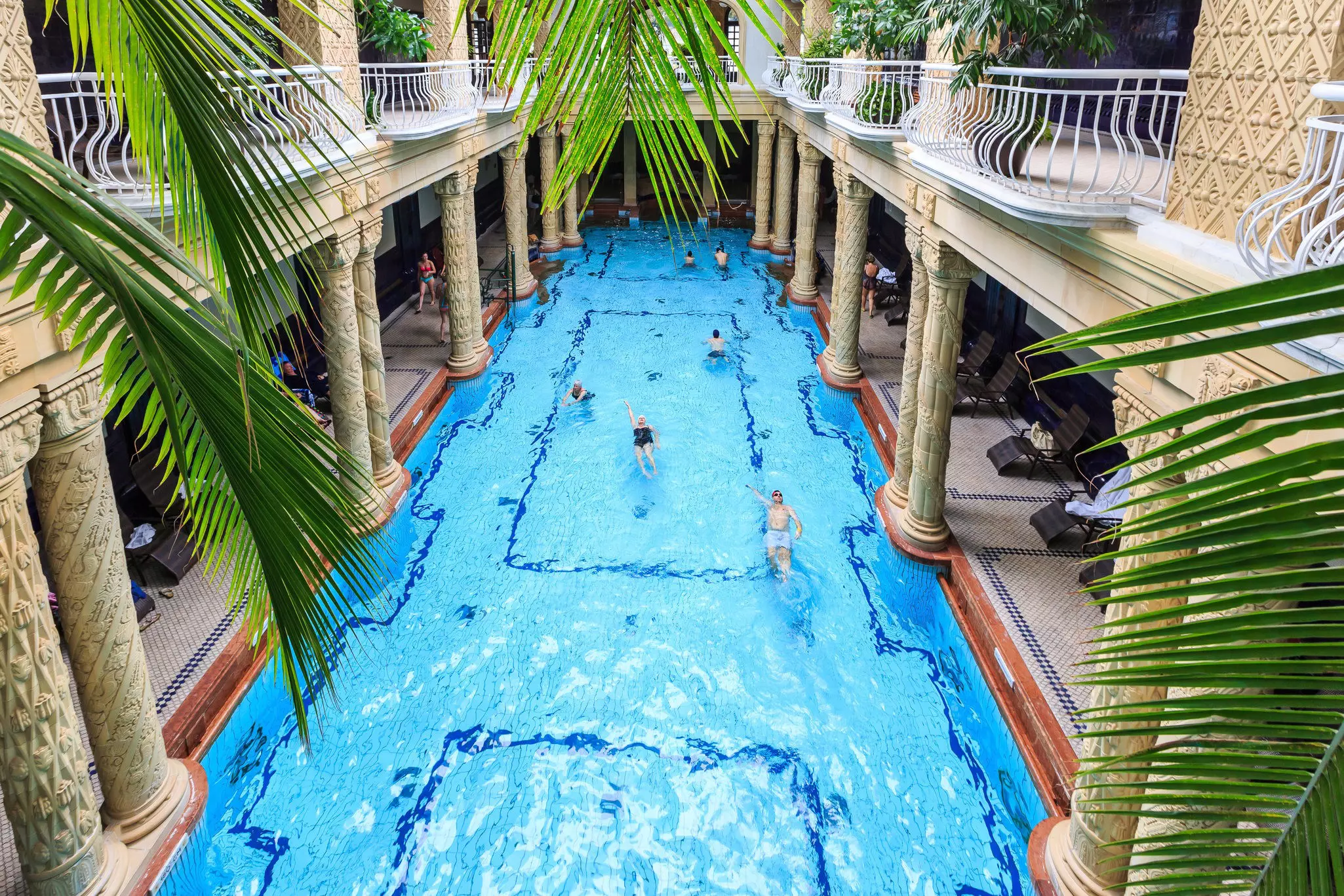 Swimmers at an indoor rectangular pool with a balcony above.