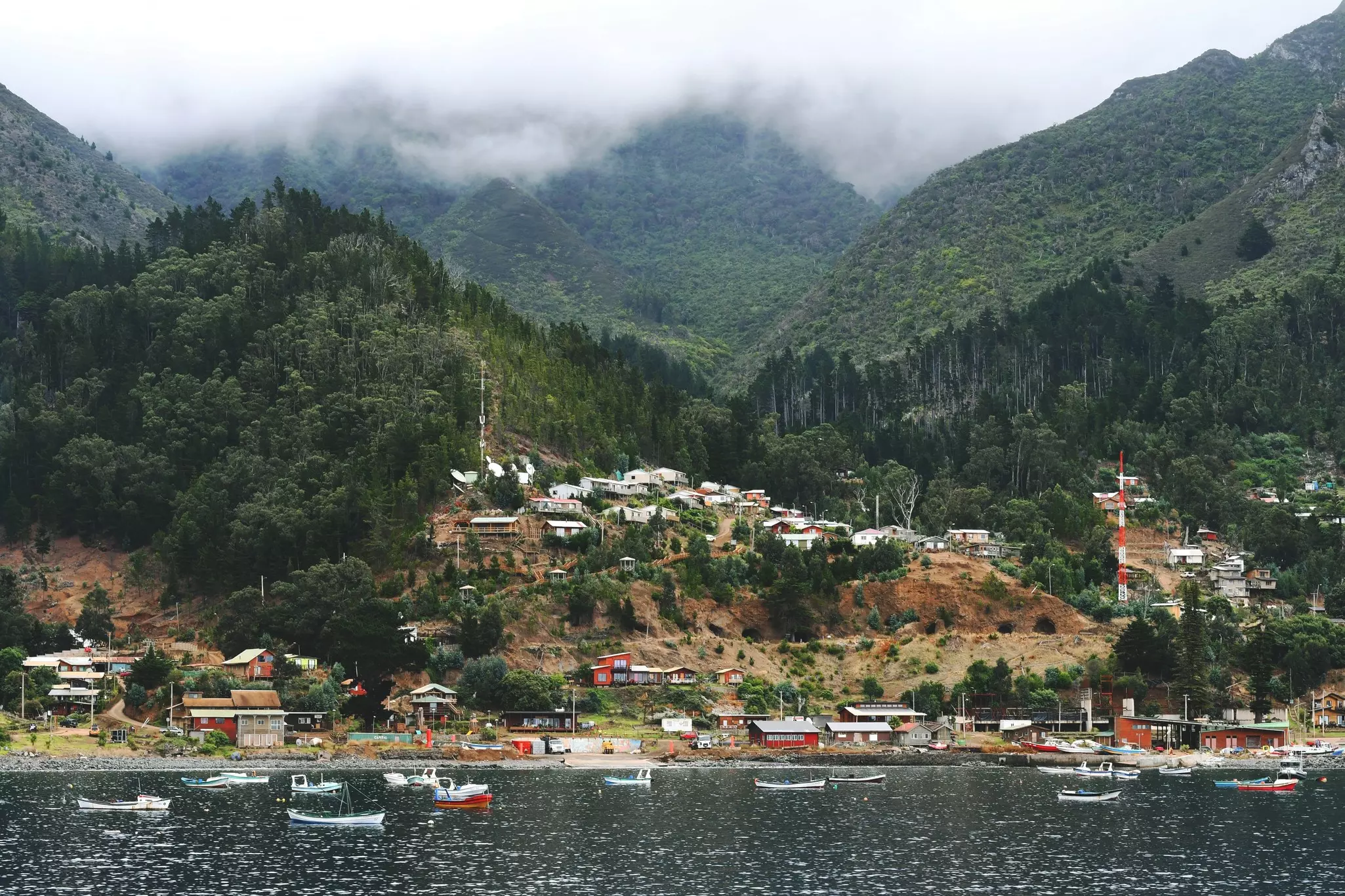A small settlement on the hills of an island with mist coming down from the peaks above