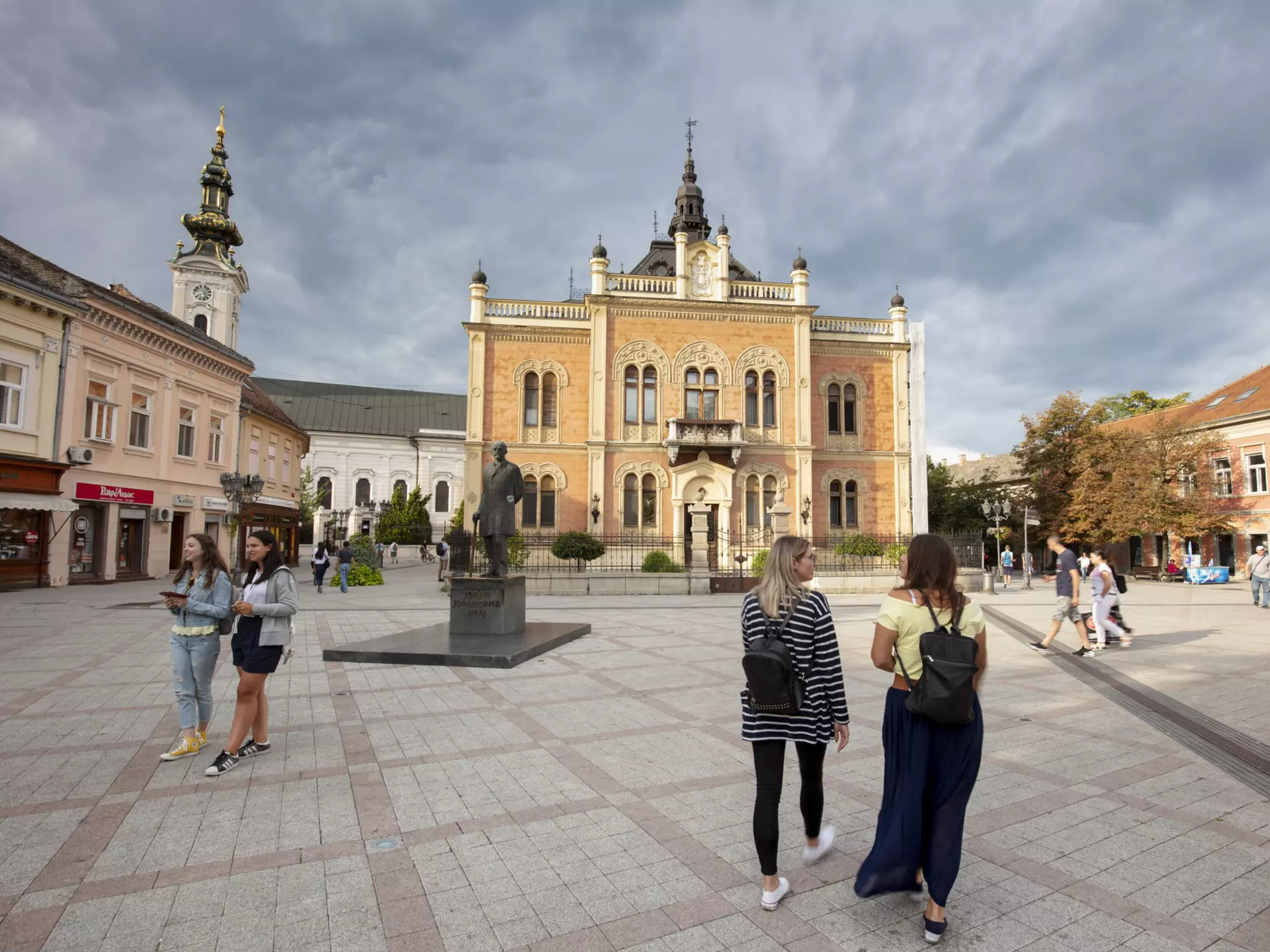 People walk across a square in front of a Baroque church building