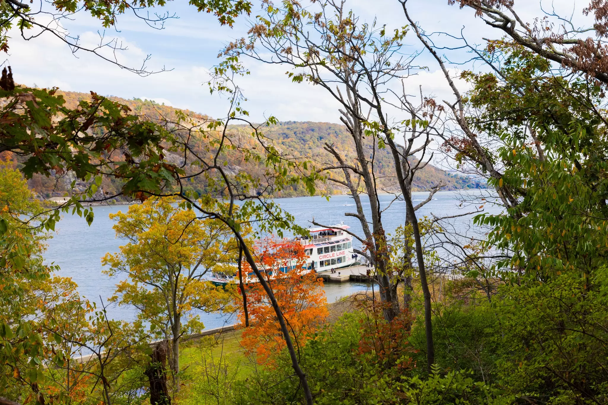 Circle Line's Oktoberfest fall foliage cruise, docked on the Hudson River at Bear Mountain State Park. View from inside the park of the river, with fall foliage framing the boat.