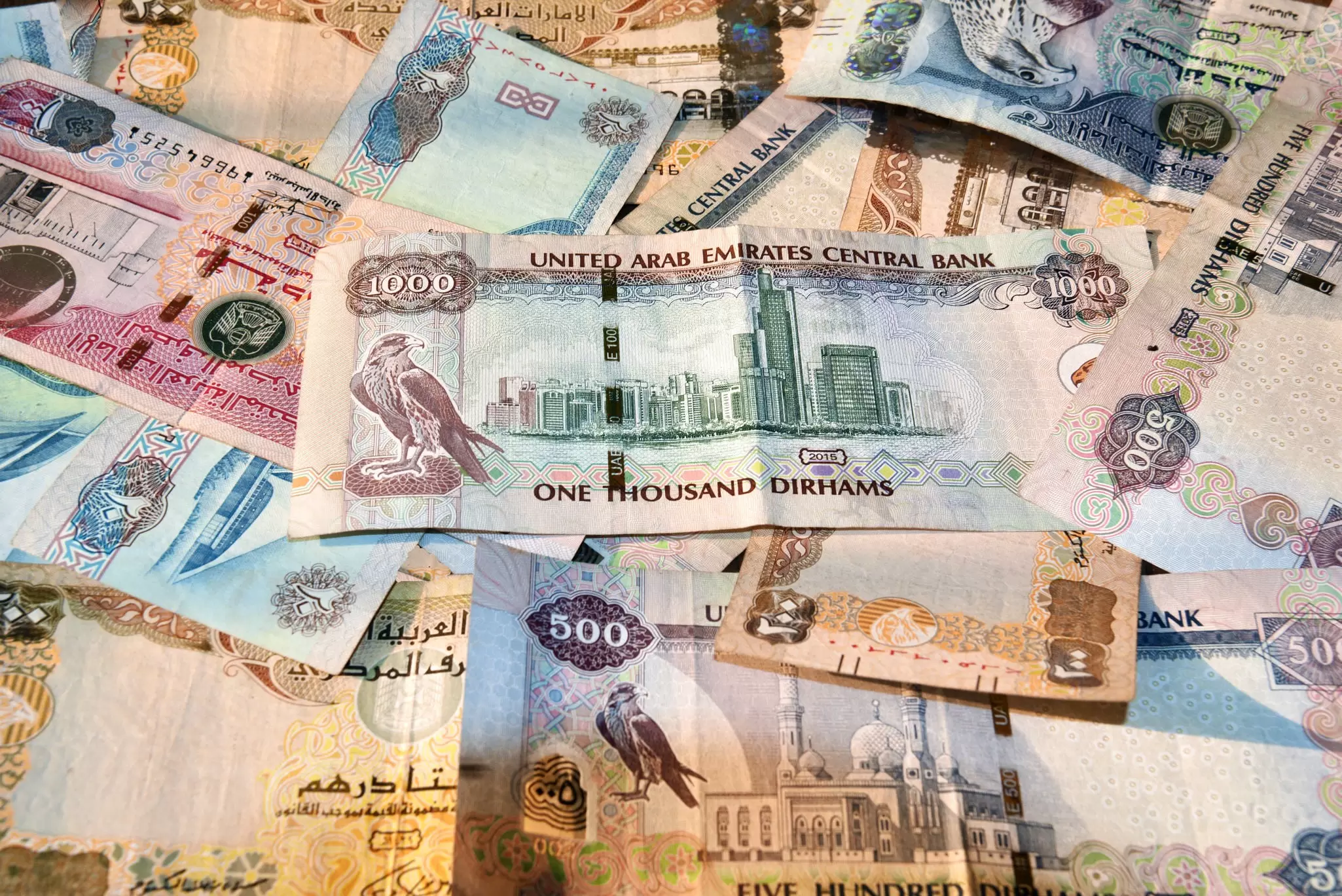 A scattered pile of United Arab Emirates dirham banknotes, with a 1000 dirham note showing a city skyline on top