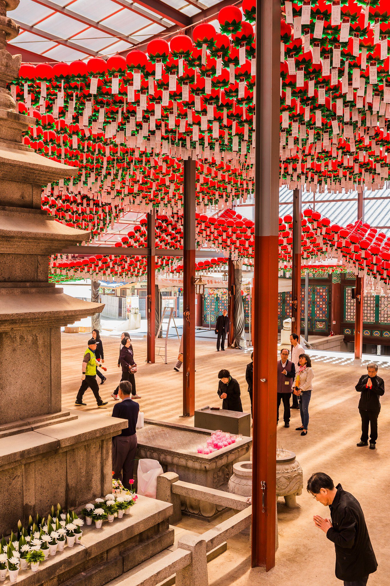Hundreds of red lanterns with white paper tags hanging over a temple courtyard where people stand praying, Bongeunsa, Seoul.
