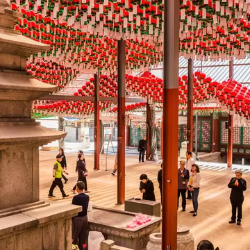 Hundreds of red lanterns with white paper tags hanging over a temple courtyard where people stand praying, Bongeunsa, Seoul.