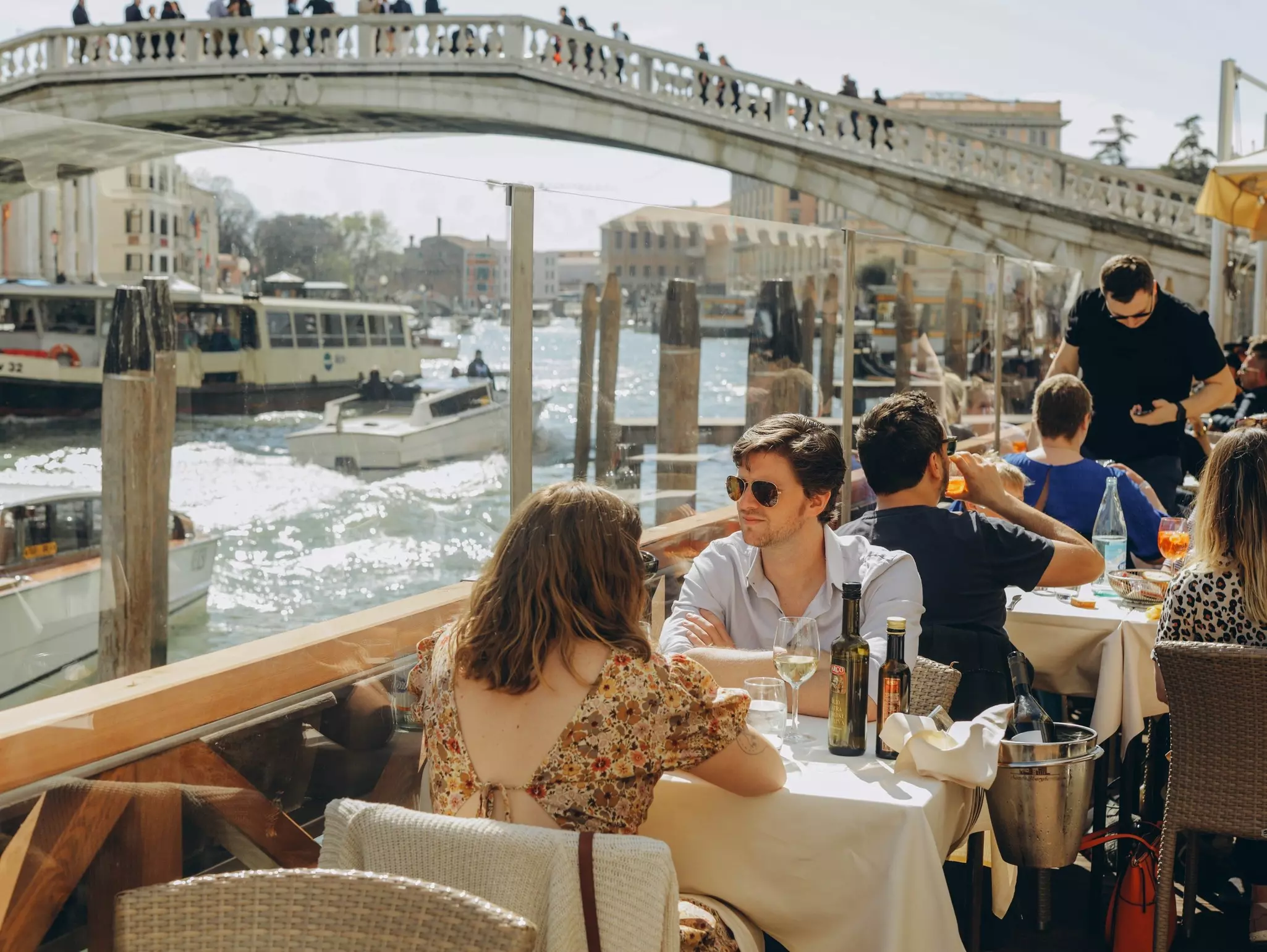People are sitting at the outside terrace of a small cafe in Venice, Italy.