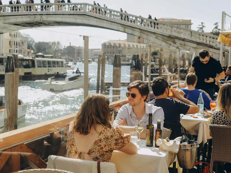 People are sitting at the outside terrace of a small cafe in Venice, Italy.