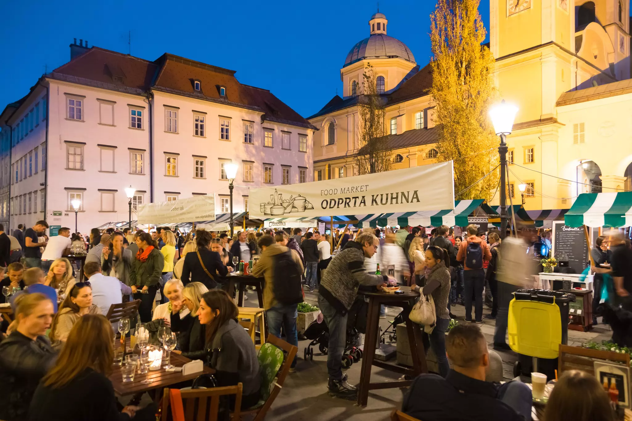 People dine at tables beside food stalls at an open-air culinary night market.