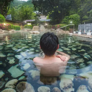 A person sitting in a clear outdoor pool lined with rocks.