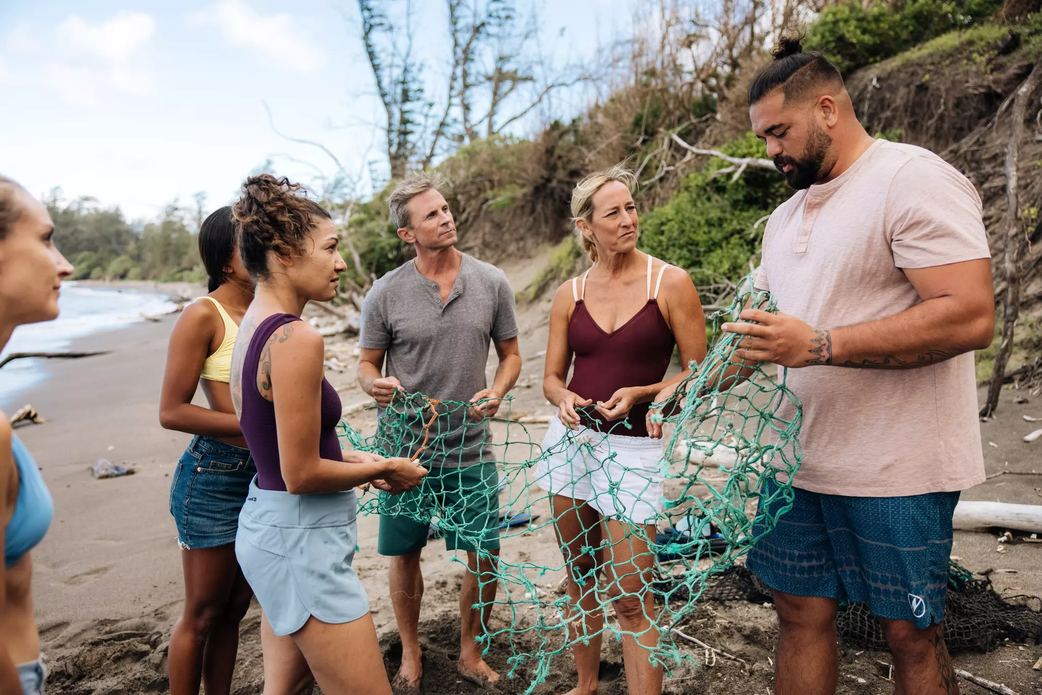 A man shows a group of men and women volunteers an abandoned net on a beach on an overcast day.