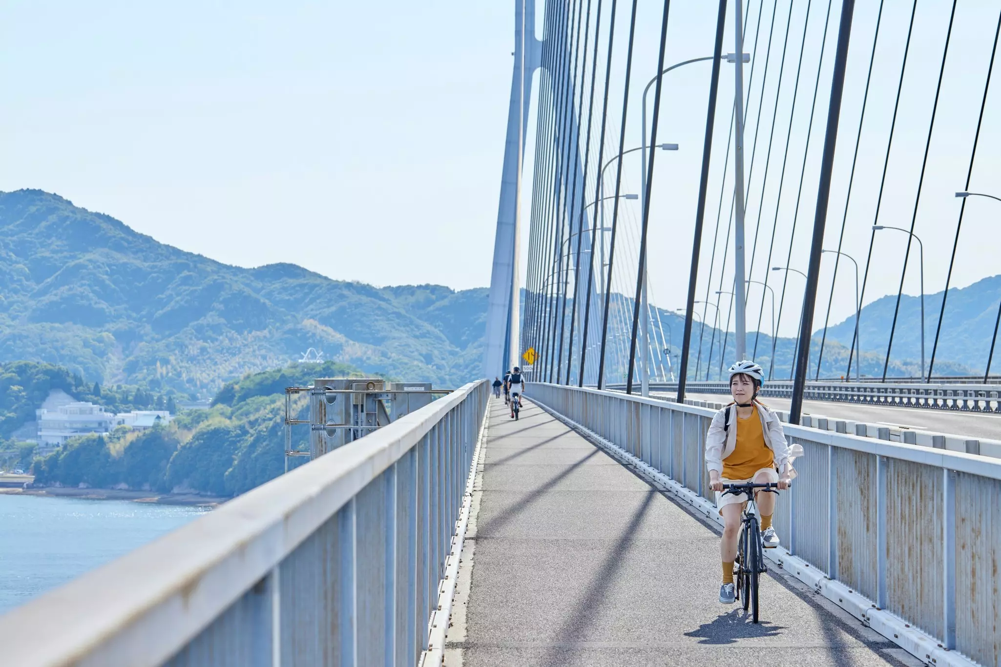 A woman pedals in the bike lane of a bridge over a body of water.
