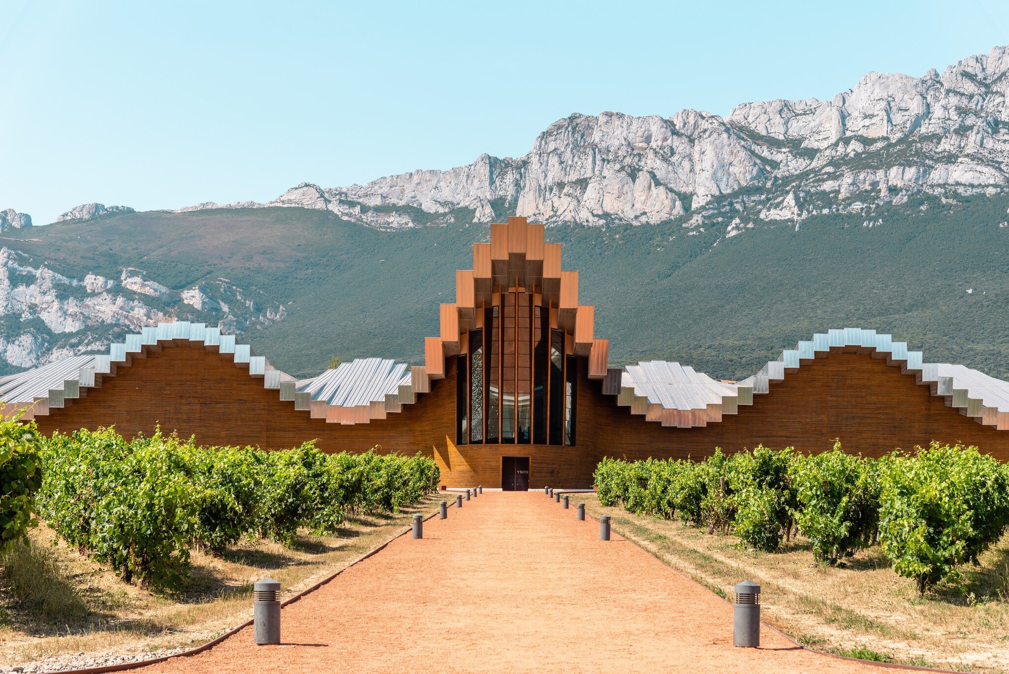 A building with a wave-like roof structure and chapel-like entrance at the foot of some mountains.