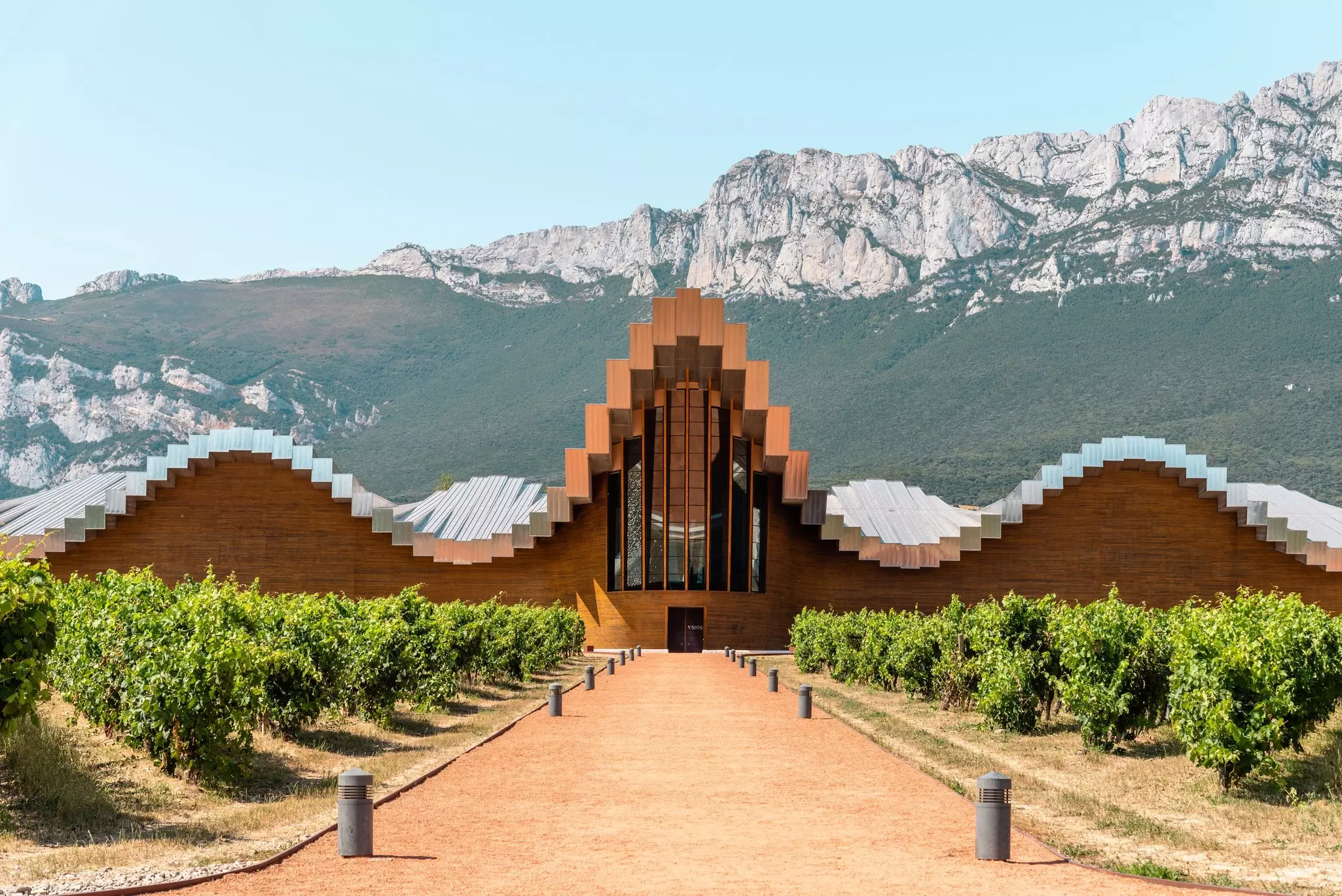 A building with a wave-like roof structure and chapel-like entrance at the foot of some mountains.