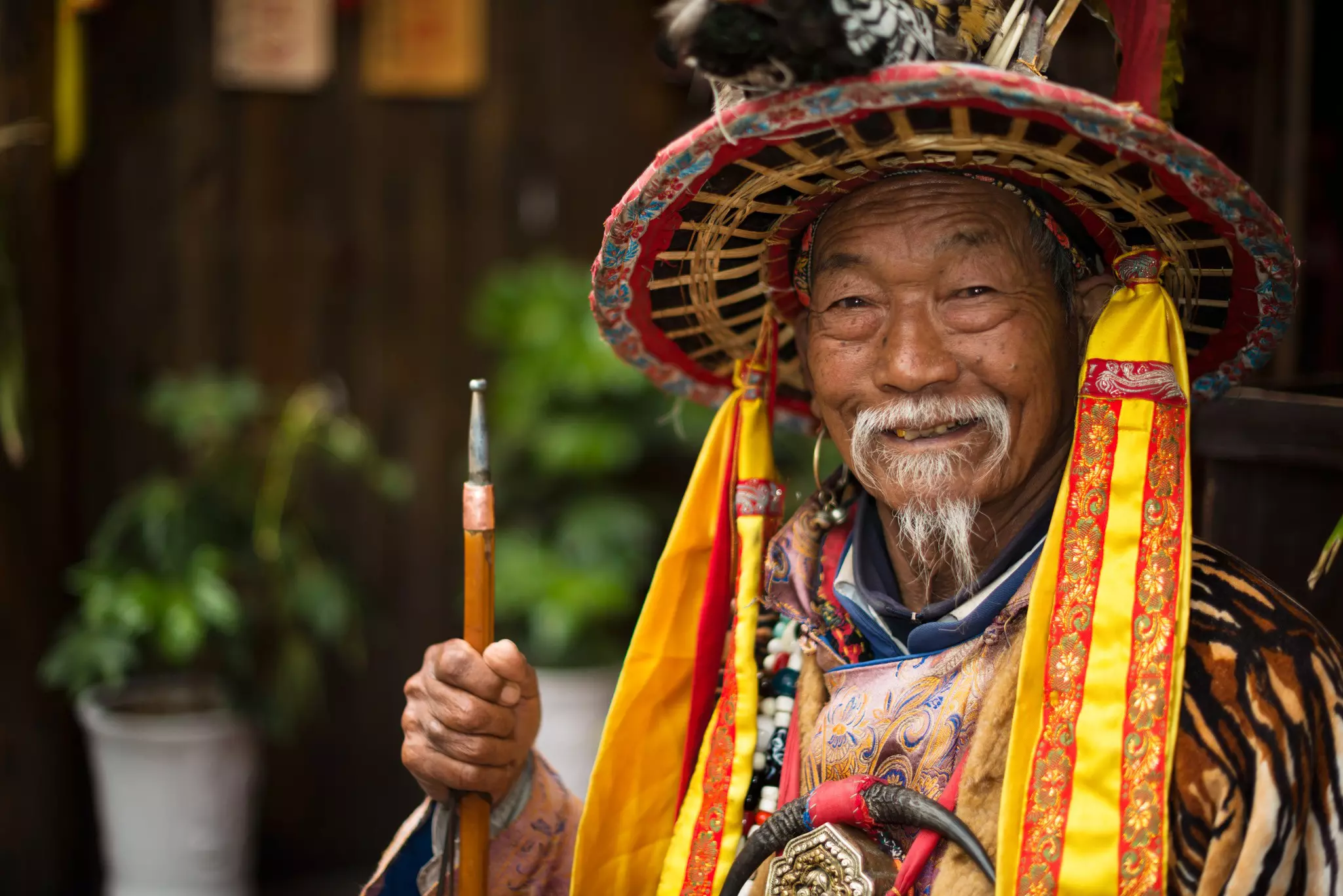 A Naxi nationality old man dressed in ancient Dongba clothing, smiling and welcome the travelers