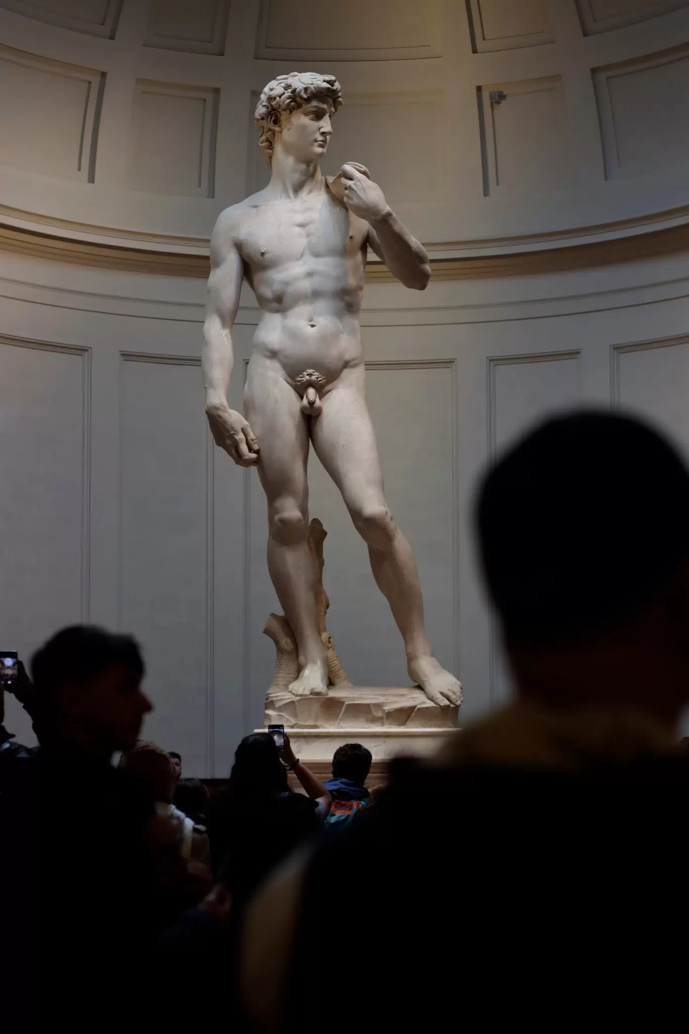Statue of a naked man in a museum surrounded by observers