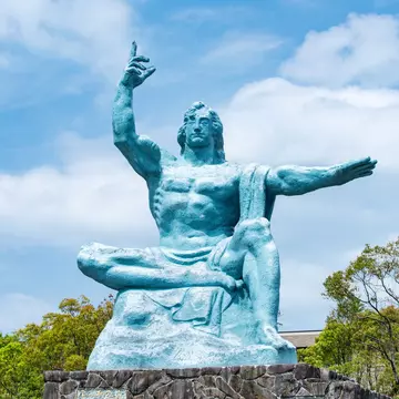 A large blue-green seated statue with one arm raised and one outstretched.