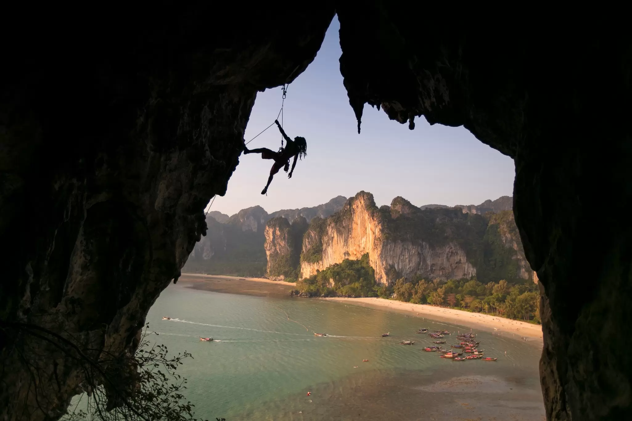View of a climber climbing the rock wall at sunset with the beautiful Railay beach in the background in Krabi Province, Thailand.   