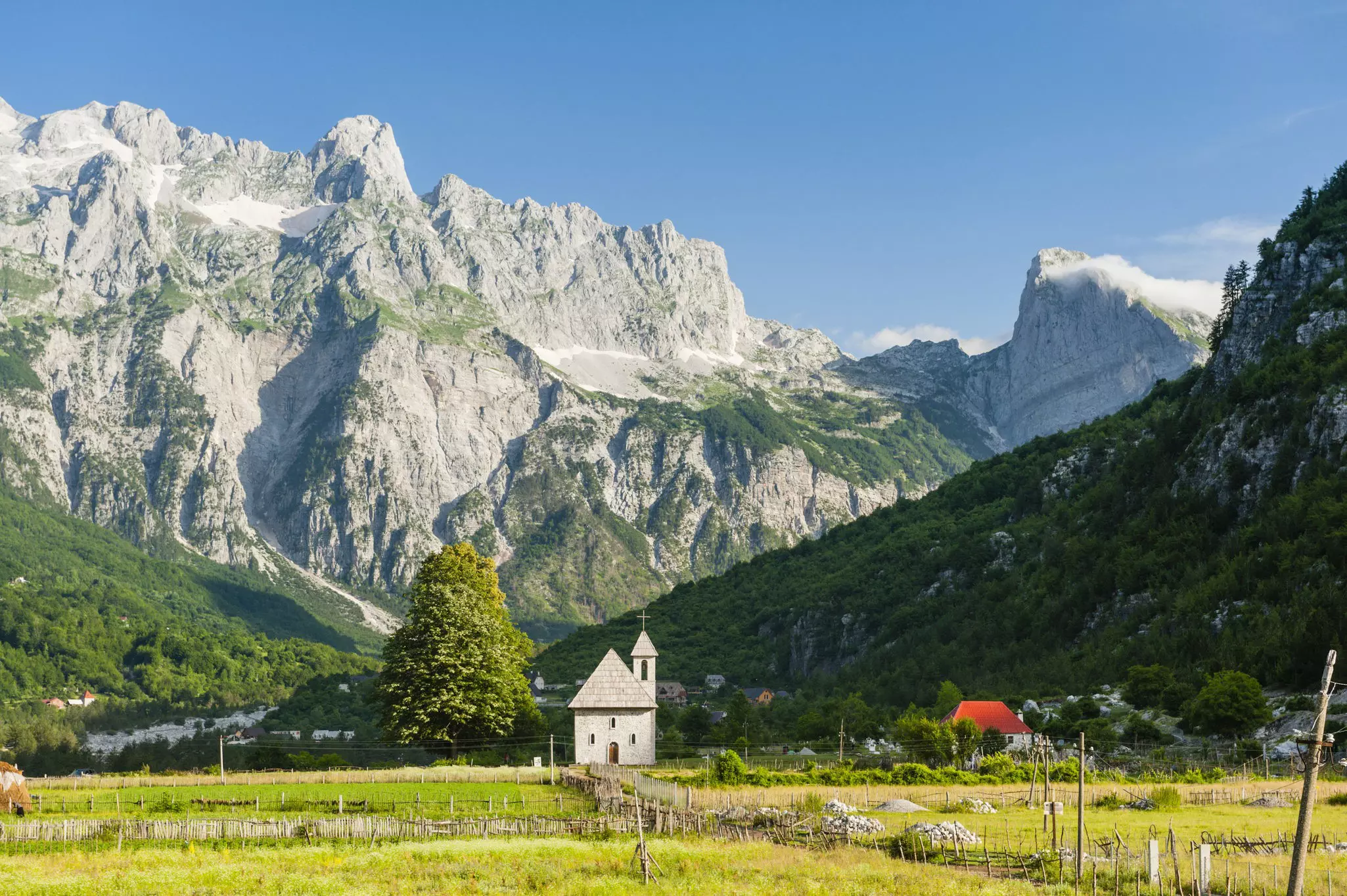 A very small church at the edge of farmland and the foot of jagged mountain peaks.