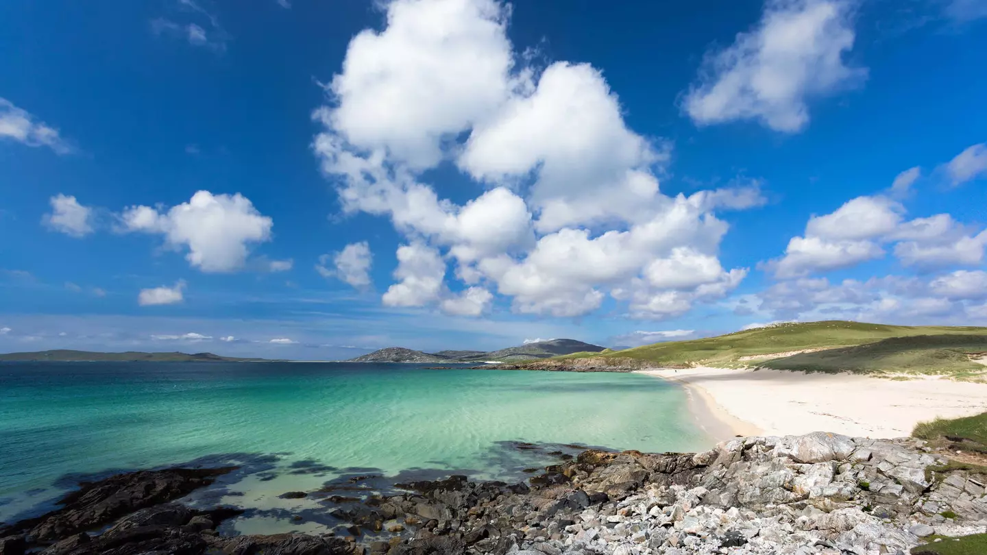 Turquoise waters meet a wide stretch of empty beach on a sunny day.