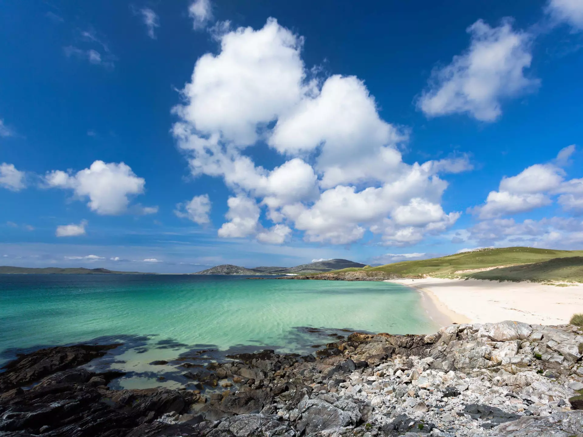 Turquoise waters meet a wide stretch of empty beach on a sunny day.