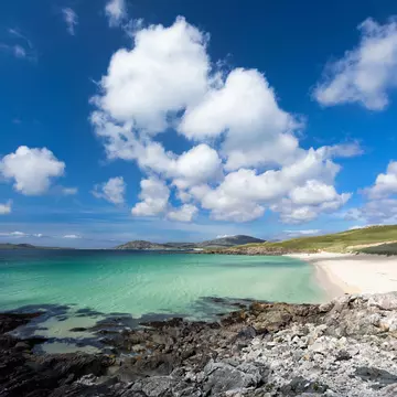 Turquoise waters meet a wide stretch of empty beach on a sunny day.