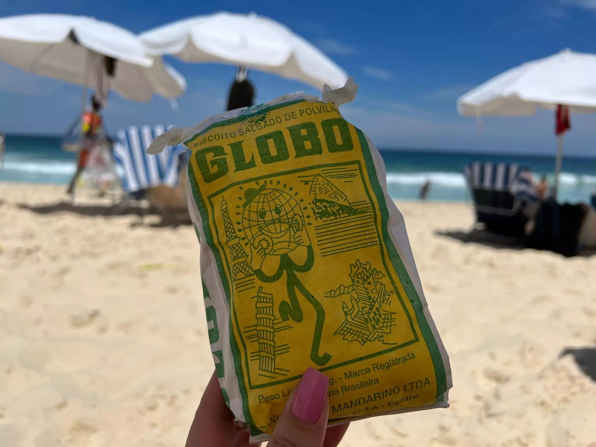 Rio de Janeiro, Rio de Janeiro, Brazil - March 4, 2023: A woman holds a pack of iconic Globo cookies by the beach, capturing the perfect snack moment with the ocean in the background.