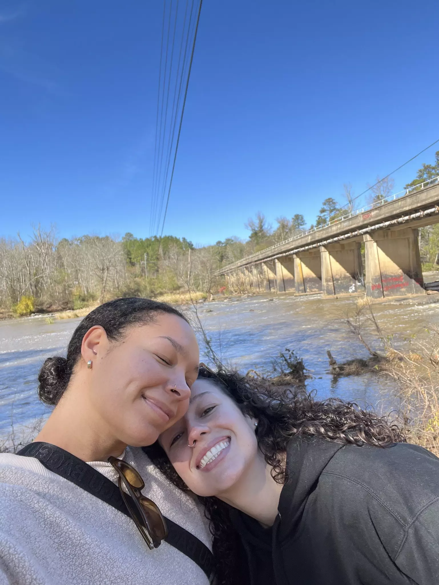 Two women cuddle on the banks of the river.