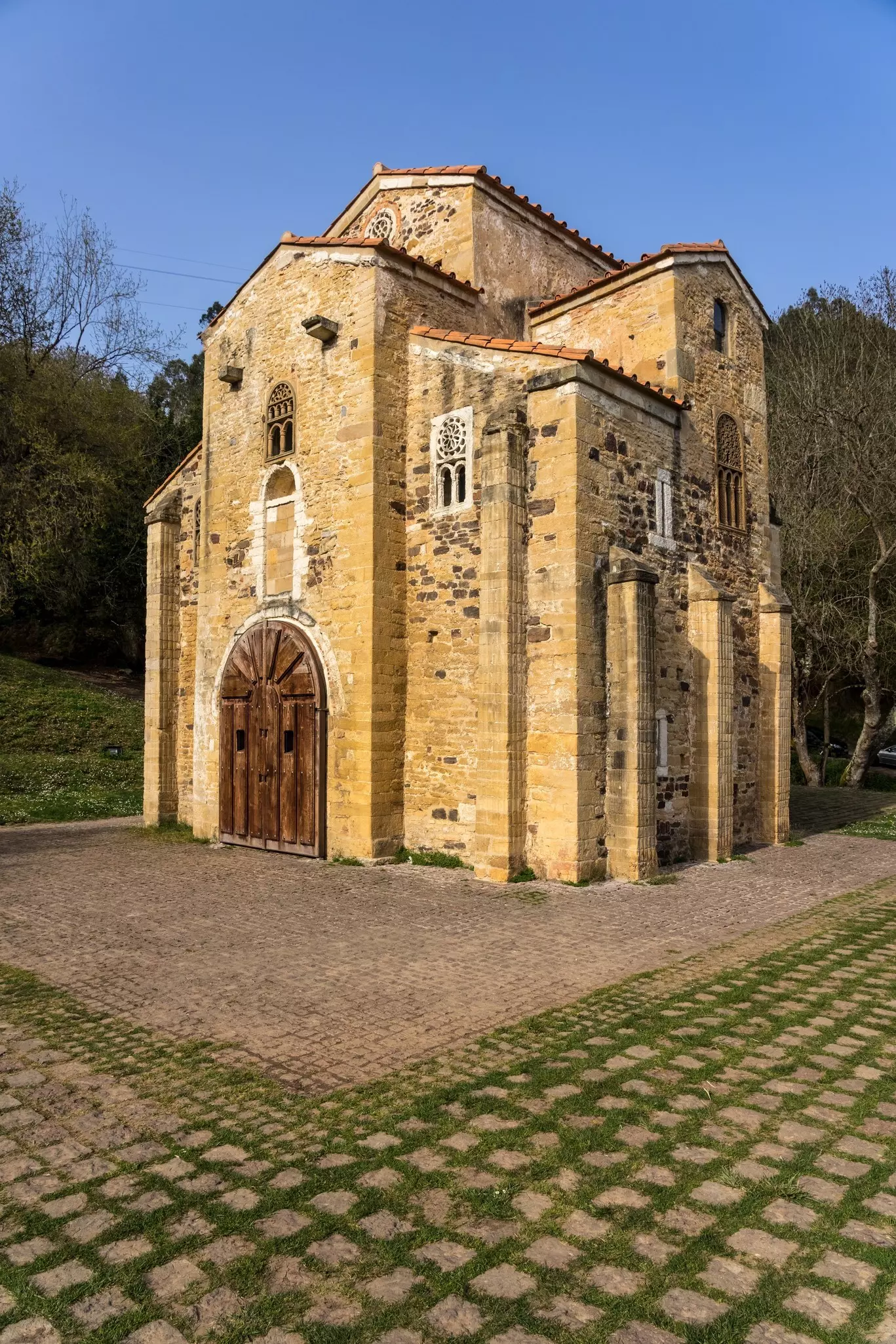 Facade of the Church of San Miguel de Lillo in the mount of Naranco at sunset. Oviedo, Asturias, Spain with blue skies and winter trees behind it.