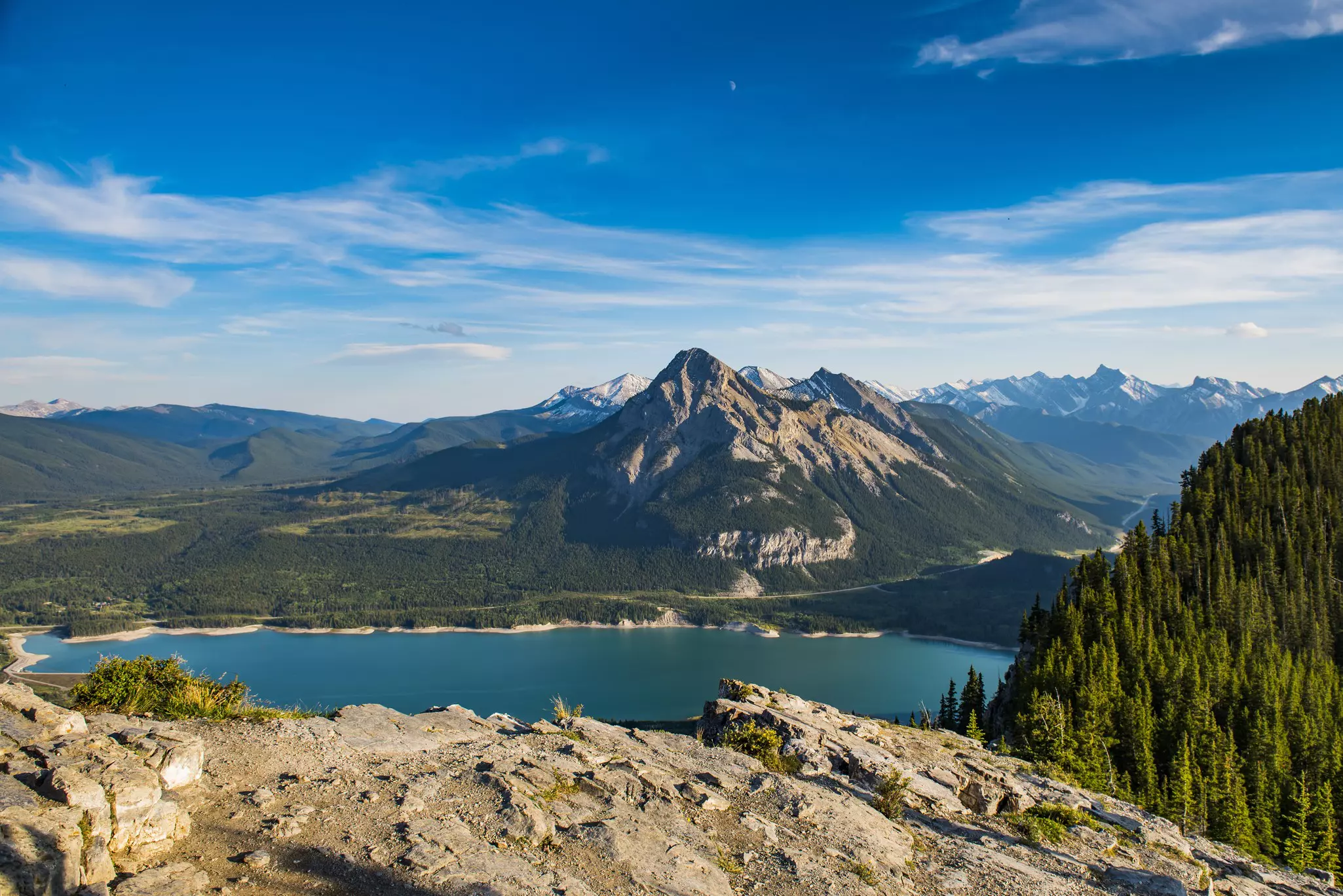 A rocky overlook of a blue lake with mountains on the other shore.