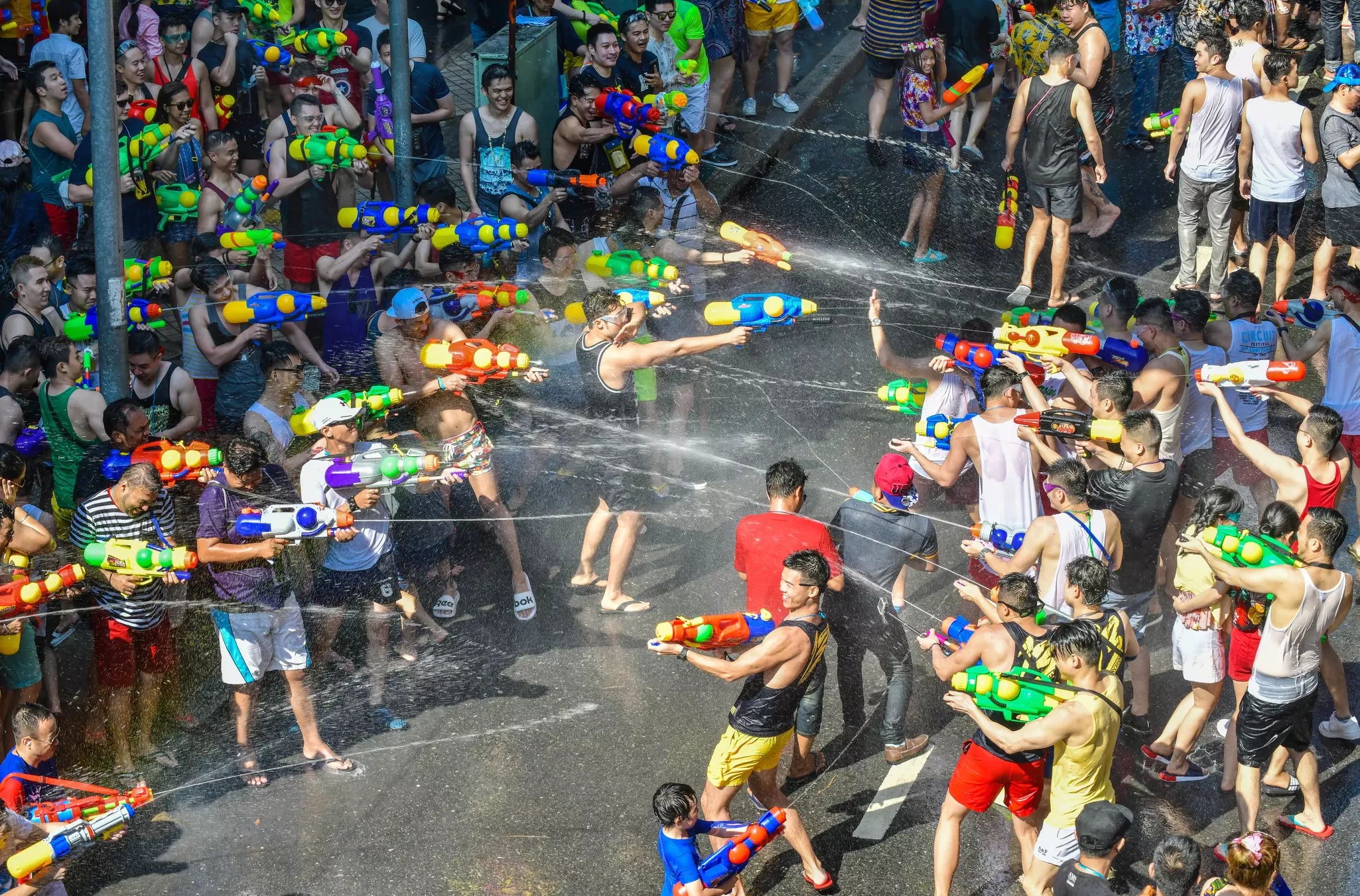 A huge water fight in the street with people armed with water pistols shooting at each other and laughing.