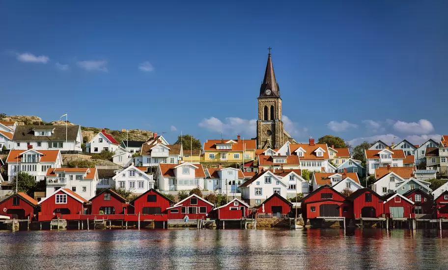 Red waterfront boathouses and white houses below a church spire in a Swedish coastal fishing village.