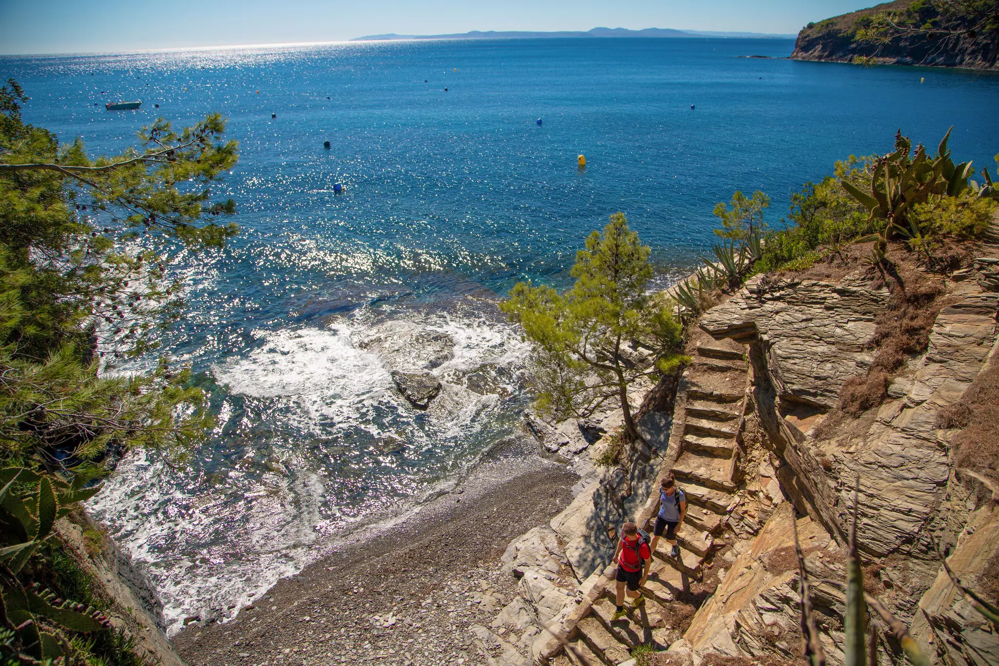 Two hikers walk down steps to a secluded stony beach