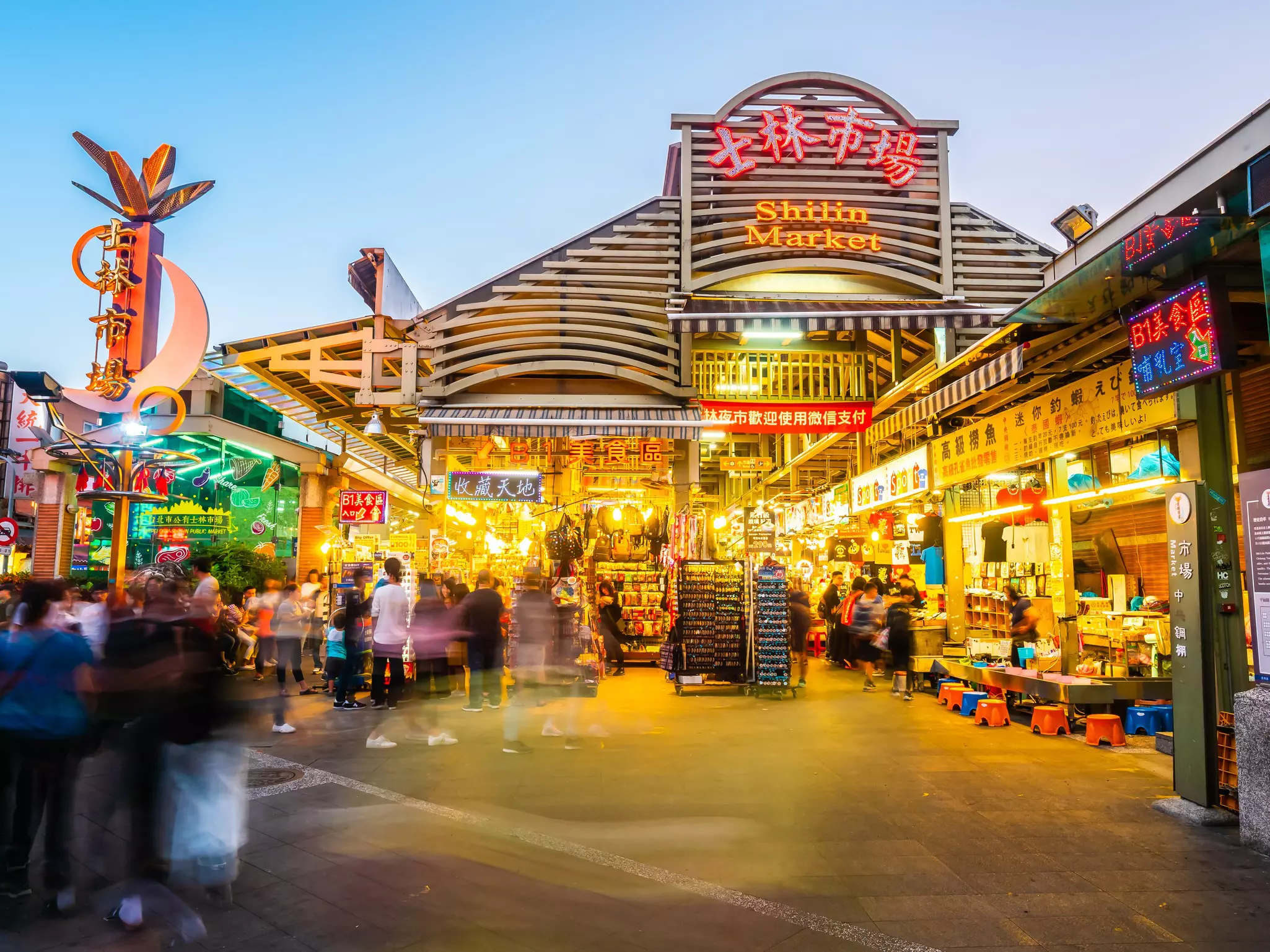 People enter a large covered food market as dusk falls