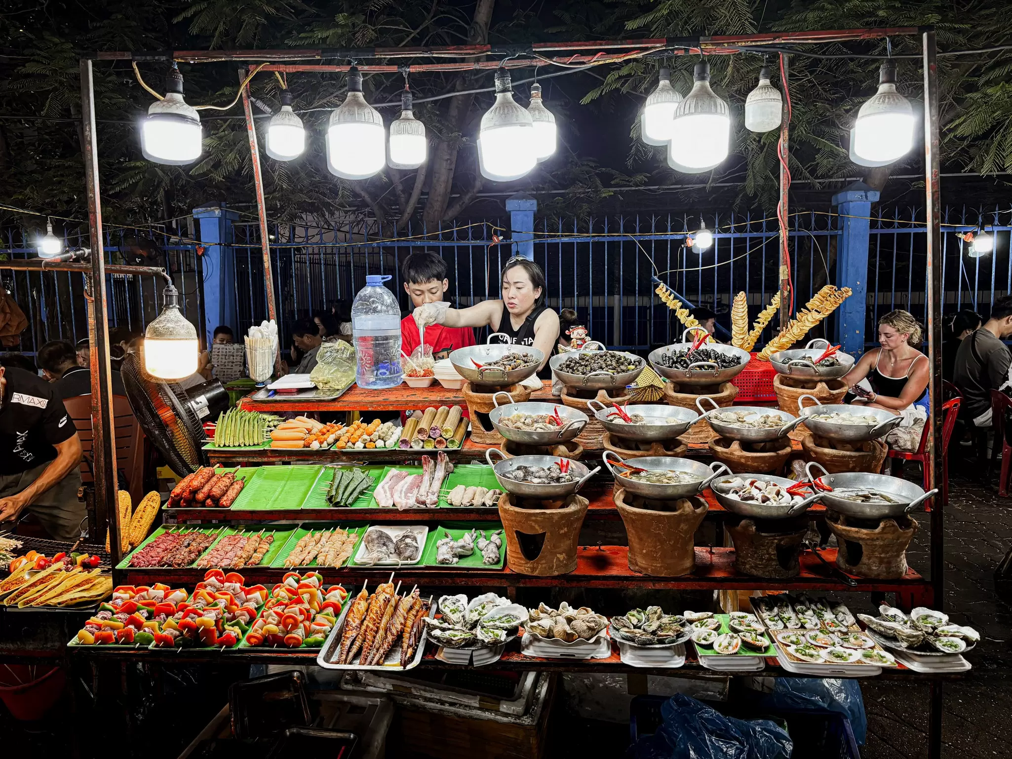 A vendor mans a stall piled with various street foods at a night market in Danang, Vietman