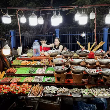 A vendor mans a stall piled with various street foods at a night market in Danang, Vietman
