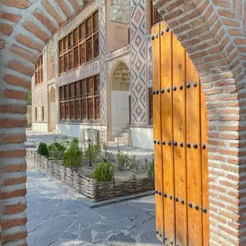 Ornate palace facade with blue and red tilework and wooden lattice windows, framed by a brick arch and door.