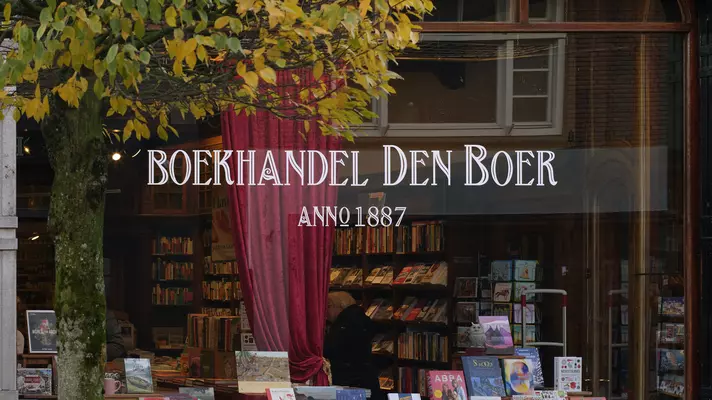 The window of a bookstore. A red curtain is draped across the window, partially blocking the view of the floor to ceiling bookshelves.