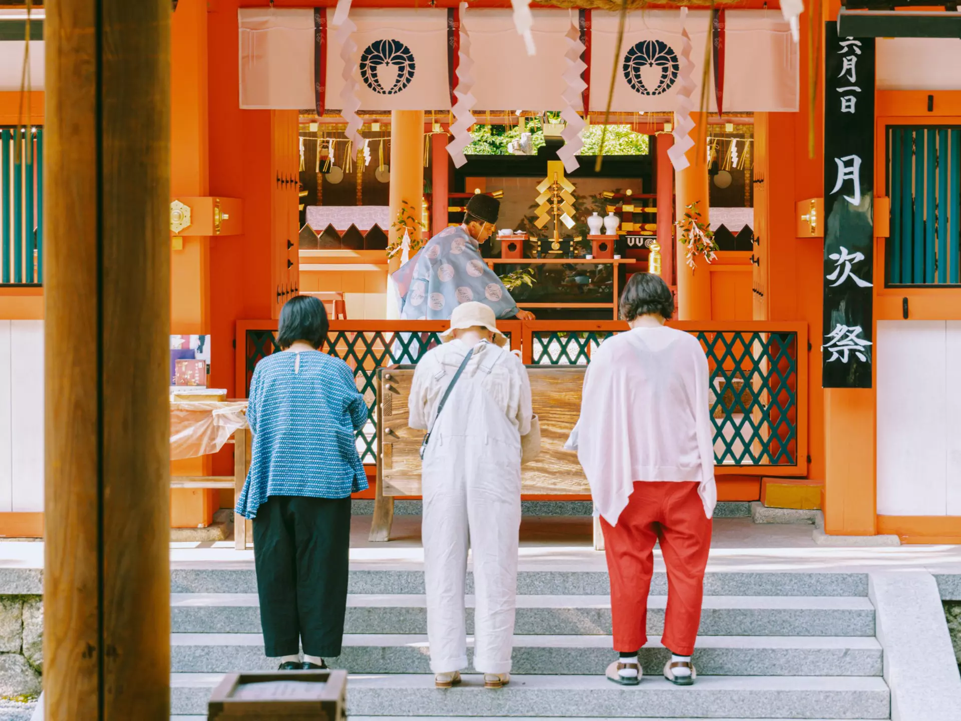 Three women wait on steps outside a tea shop at a market.