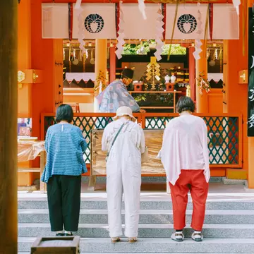 Three women wait on steps outside a tea shop at a market.