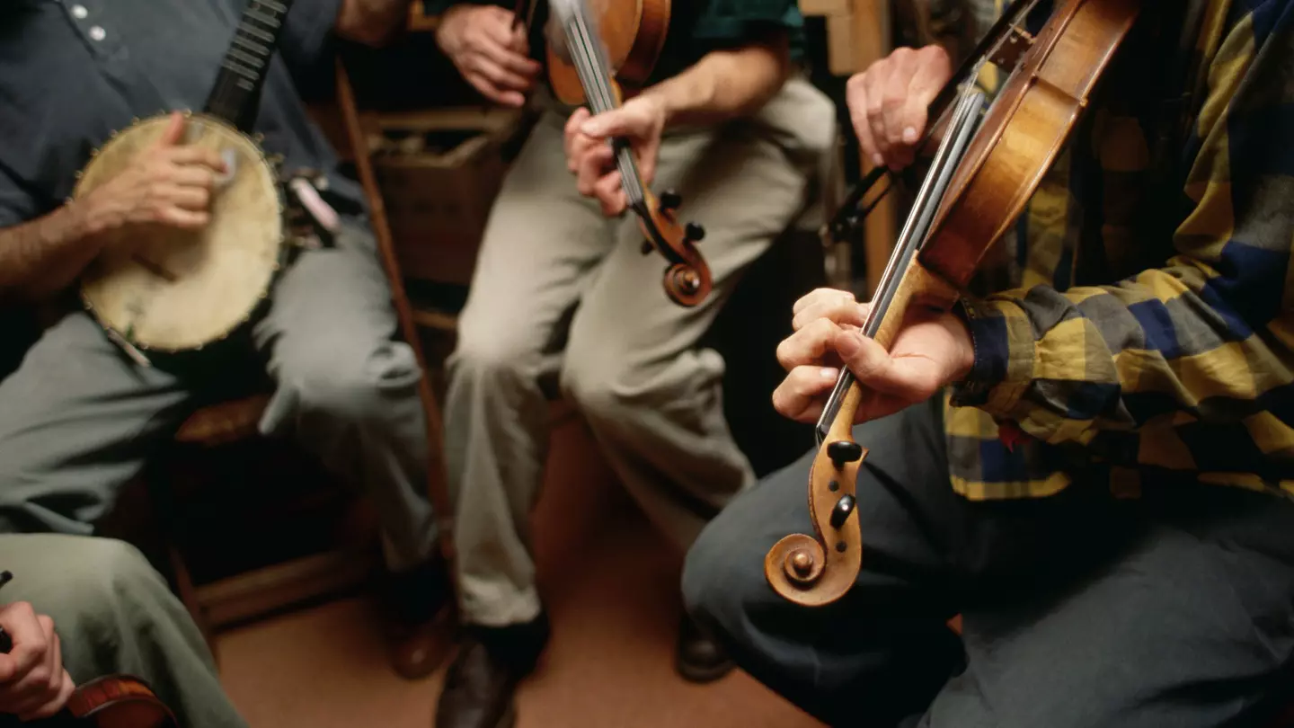 Three musicians play a banjo and two violins in a bluegrass style