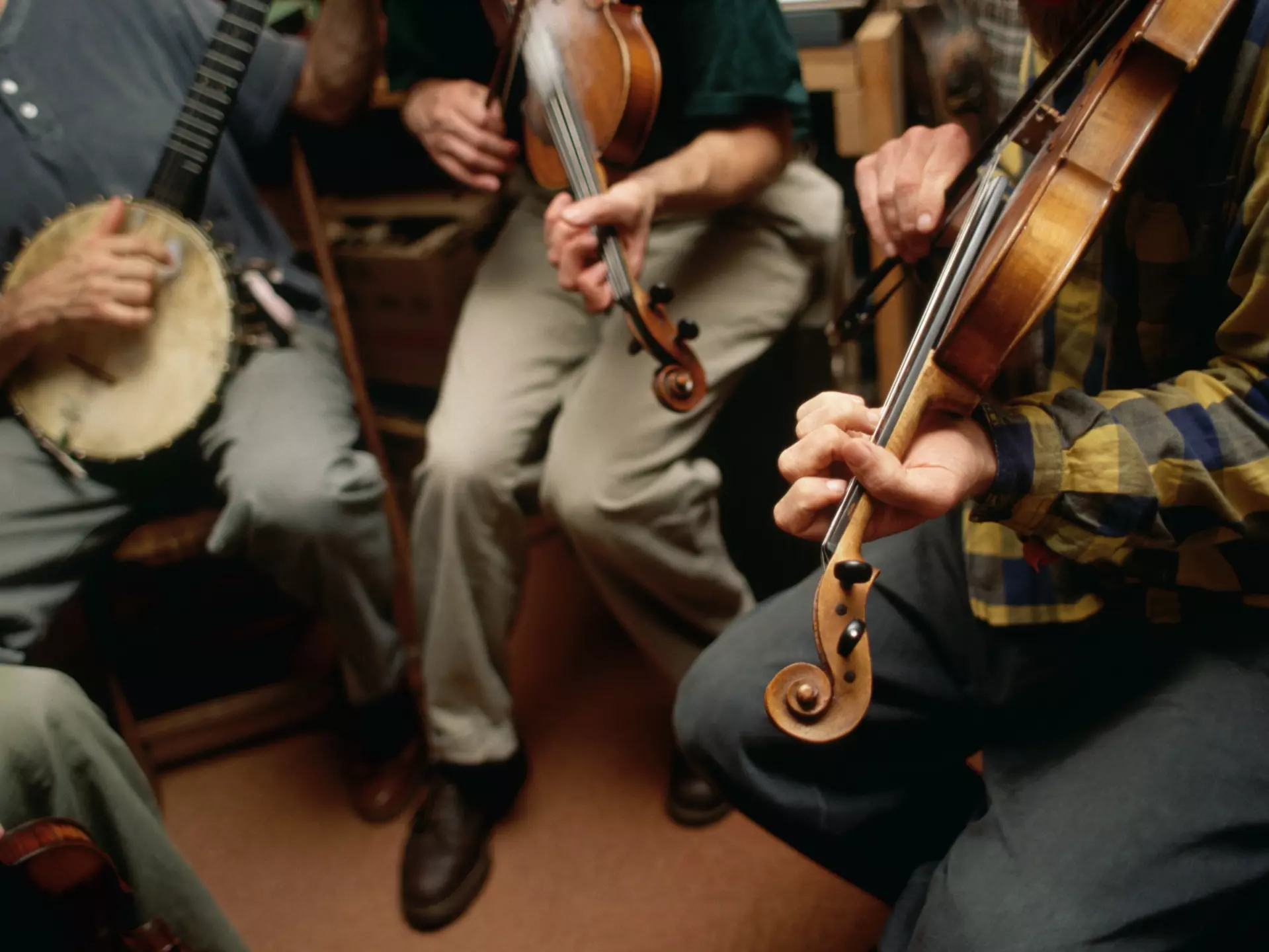 Three musicians play a banjo and two violins in a bluegrass style
