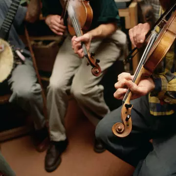 Three musicians play a banjo and two violins in a bluegrass style