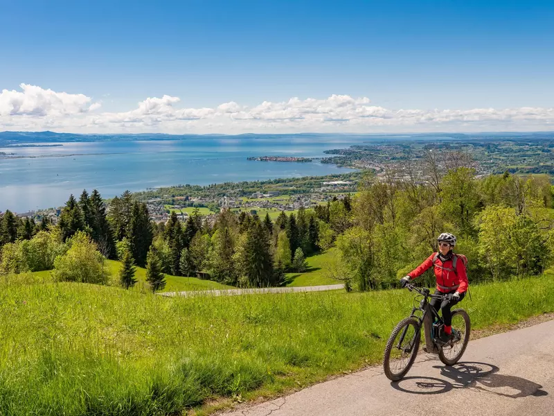 Woman in a red jacket and white helmet on a cycling path above a lake