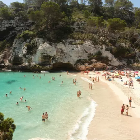 People sunbathe and swim on a white-sand beach