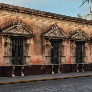 Casa de Montejo, Mérida: weathered ochre facade with barred windows framed by carved figures and heraldic pediments