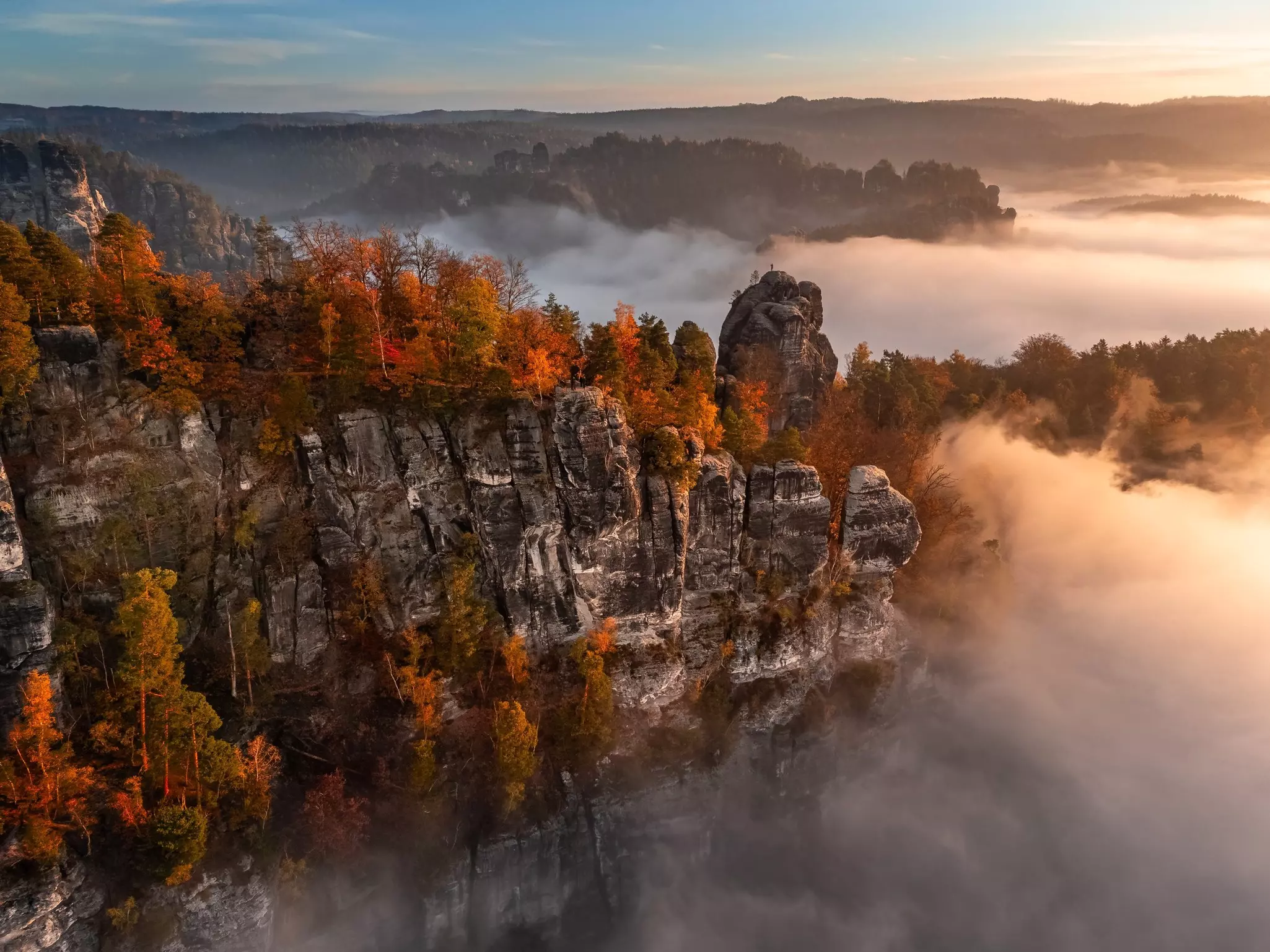 A rocky outcrop at dawn on a foggy morning in autumn, with golden colored leaves in the trees.
