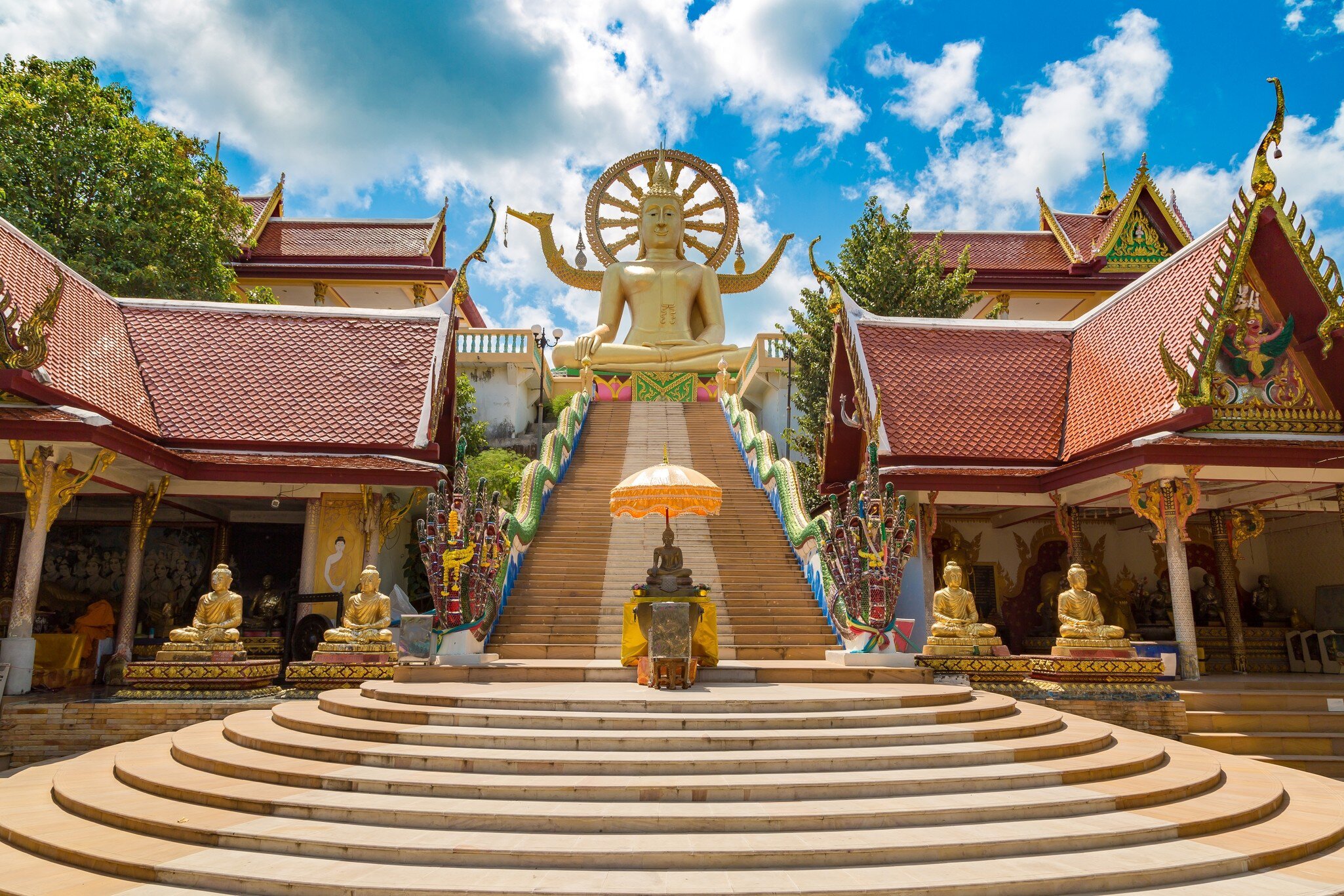 Steps leading up to the Big Buddha statue in Wat Phra Yai, Koh Samui, Thailand, on a summer day with bright blue sky.