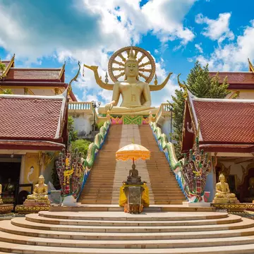 Steps leading up to the Big Buddha statue in Wat Phra Yai, Koh Samui, Thailand, on a summer day with bright blue sky.
