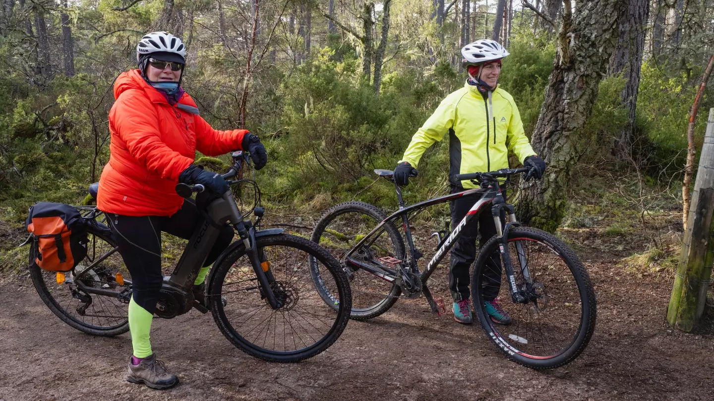 Two cyclists in the woods carry their bikes during a cyclocross race at Russian Jack Springs Park
