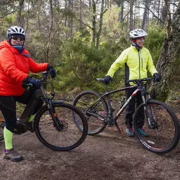 Two cyclists in the woods carry their bikes during a cyclocross race at Russian Jack Springs Park