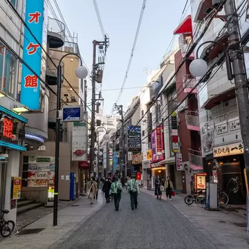 Pedestrians on a shop-lined street near Sannomiya in Kobe, Japan, under neon signs and tangled overhead wires