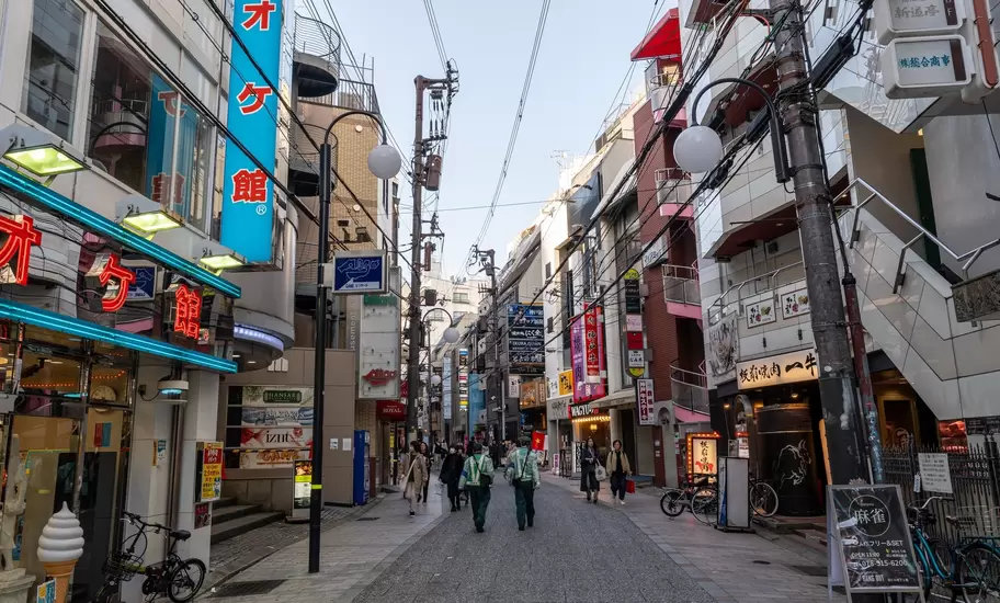 Pedestrians on a shop-lined street near Sannomiya in Kobe, Japan, under neon signs and tangled overhead wires